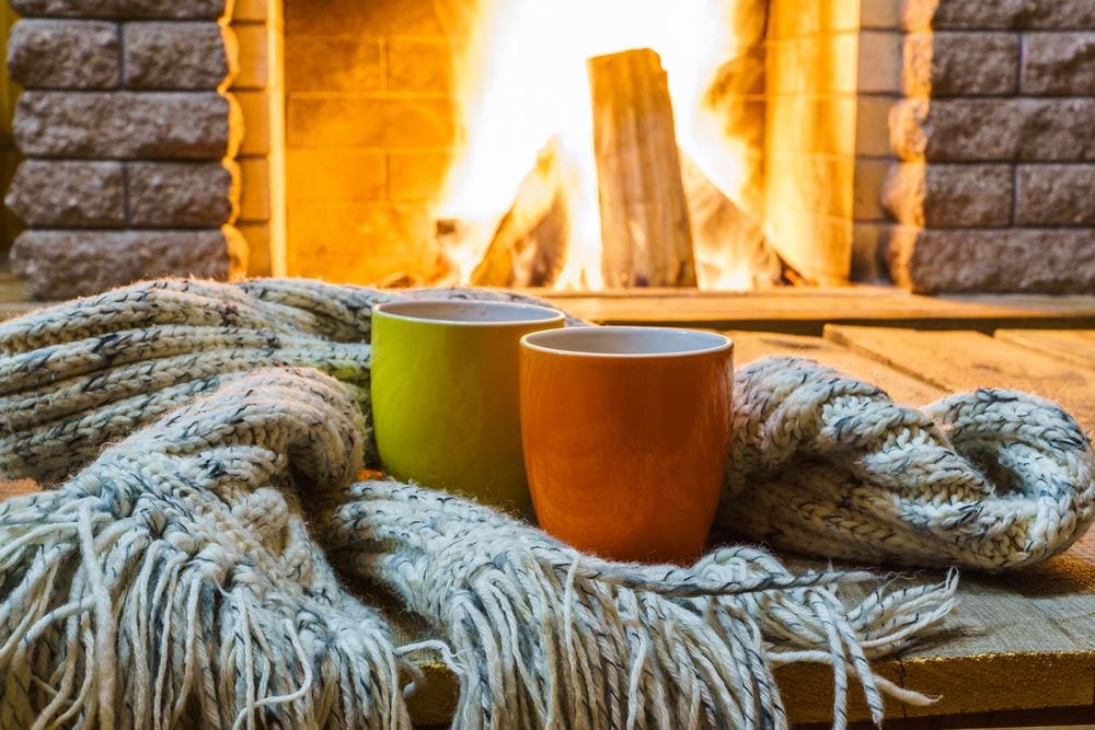 two mugs for tea or coffee, woolen things near cozy fireplace