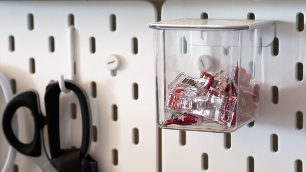 Close up on clips stored inside a clear box hanging from peg board